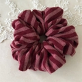 Close-up of a striped knit scrunchie in burgundy and pink with soft lace details - Red