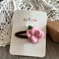 Detail of pink wool felt flower hair clip with green leaves on Aidou display card - Flower