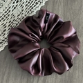 Macro detail of bordeaux satin scrunchie showing glossy texture and label on gray wood - Faux Leather Burgundy