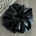 Macro detail of high-shine black satin oversized scrunchie with elegant logo tag on wood - Faux Leather Black