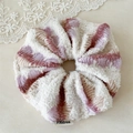 Detail of a knit scrunchie with beige and purple gradient colors and a brand tag - White