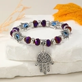 Vista de detalle de pulsera de cuentas moradas con mano de Fátima y ojo turco en piedra blanca - Púrpura