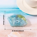 Pince à cheveux poisson en acétate marbré bleu-vert sur fond de plage d'été - Conque