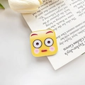 Süße gelbe quadratische Emoji-Haarklammer mit Überraschungsgesicht auf offenem Buch - Benommen