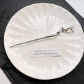 Silberne Haarnadel aus Flüssigmetall mit Wellendesign auf weißem Keramikteller - Flüssiges Silber