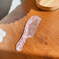 Elegante peine de acetato con dientes anchos y textura de mármol rosa y blanco en mesa - Rosa Melocotón