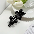 Matte black floral hair clip with round bead accents on a minimalist white table - Black