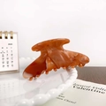 Amber marble acetate hair claw clip with brown and cream patterns on a ceramic tray - Brown