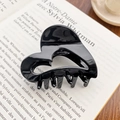 Glossy black heart-shaped hollow hair claw clip made of premium acetate on a book - Solid Black