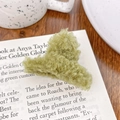 Pinza para el pelo de felpa verde hierba sobre una revista con una taza de cerámica detrás - Verde Matcha