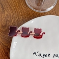 Französische weinrote Katzen-Haarklammer mit Goldlogo auf edlem Holz- und Keramikgrund - Katze-Weinrot