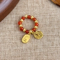 Detalle de anillo de cuentas rojas y doradas con dijes Fu sobre textura tejida - Estilo B Riqueza (Fu)