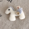 Detailed macro view of cream felt pony brooch with wooden button and wings on linen - White Pony (27870D)