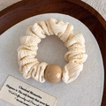 Dettaglio di scrunchie in tessuto plissettato crema con perla beige liscia su sfondo - Beige