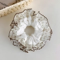 Detailaufnahme von Blumen-Spitzen-Scrunchie mit braunem Rüschenrand auf Elfenbeingewebe - Brauner Muschelsaum Blumenstil