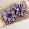 Primo piano di due elastici scrunchie viola a fiori in tessuto su un cesto intrecciato - Set da 2 pezzi / Floreale Viola