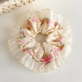 Gedetailleerde close-up van een bloemen scrunchie met kant, roze knopen en handgemaakt label - Roze Bloemen Ronde Stijl