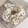 Gros plan d'un chouchou beige à pois avec bords ondulés et texture en satin soyeux - Beige à Pois Noirs