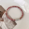 Gros plan de perles en pierre naturelle rose et charme rectangulaire aux motifs tibétains - Pierre à Veines Rouges