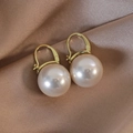 Macro detail of champagne pearl leverback earrings on elegant beige silk fabric - White