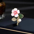 Elegante spilla a fiore dorata con smalto, strass e perla su una scatola blu scuro - Rosa