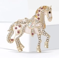 Macro dettaglio di una spilla a cavallo in smalto vintage con strass scintillanti su lega dorata - Bianco