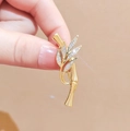Eleganter Gold-Bambus-Brosche mit funkelnden Kristallen in der Hand auf beigem Grund - Bambusknoten Form / Gold