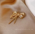 Elegante spilla a fiocco dorata con zirconi cubici su sfondo di tessuto marrone chiaro - Oro