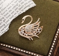 Detailed view of a gold swan brooch featuring sparkling rhinestones on a dark green box - Gold