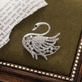 Macro shot of silver swan brooch featuring sparkling crystal inlay on green fabric - Silver
