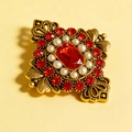 Vue détaillée d'une broche vintage ajourée avec cristal rouge et perles blanches - Rouge