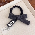 Detail of dark grey wool bow scrunchie with Nice label on a textured beige plate - Grey Black