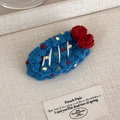 Close-up of royal blue hand-crocheted fruit hair clip with red flowers on fabric - Blue Bottom Red Bow Style (27629F)