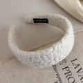 Detail eines cremefarbenen Sherpa-Stirnbands mit schwarzem Handmade-Etikett auf Leinen - Weiß