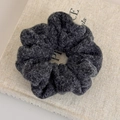Detailansicht eines dunkelgrauen Woll-Scrunchies auf grauem Hintergrund - Schwarz