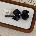Makro-Detail der eleganten Satin-Bogen-Haarspange mit luxuriösen Strasssteinen und Perle - Schwarz