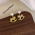 Close-up of pearl stud earrings with golden hammered rocking horse pendants on silk - Gold