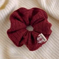 Dettaglio dell'elastico in maglia rosso vino con ciondolo a cuore su maglione beige - Borgogna