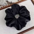 Détail d'un chouchou en tissu sergé noir avec étiquette tissée sur un plateau en bois - Noir