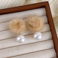 Primer plano de pendientes de pompones marrones y perlas blancas en base de madera - café