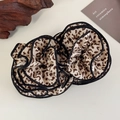 Dettaglio di due elastici scrunchie leopardati con bordo nero su uno sfondo minimalista - Leopardo Chiaro