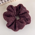 Gros plan d'un chouchou en maille bordeaux avec fils dorés sur une surface blanche - Fuchsia
