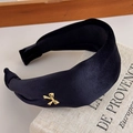 Dettaglio di un cerchietto largo in velluto nero con un piccolo fiocco in metallo dorato - Nero