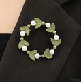 Elegante groene bladkrans broche met witte parels op een zwarte blazer revers getoond - Groene Krans Stijl