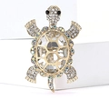 Macro shot of gold turtle brooch featuring a large clear crystal and pavé rhinestones - White