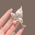 Dettaglio di una spilla a farfalla dorata con ali perlate, perle bianche e zirconi rosa - Bianco