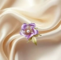 Elegante spilla a camelia viola con perla bianca e foglie verdi su sfondo di seta - Viola
