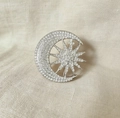 Close-up of sun and moon brooch with sparkling crystals on a textured linen fabric - Silver Star Moon