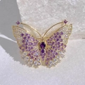 Elegant gold butterfly brooch with purple crystals and stones on a white mineral stone base - Gold