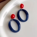 Close-up van rode en blauwe marmeren hars oorbellen op een wit keramisch bord - Ovale Knopjes (27259A) / Rood Blauw
